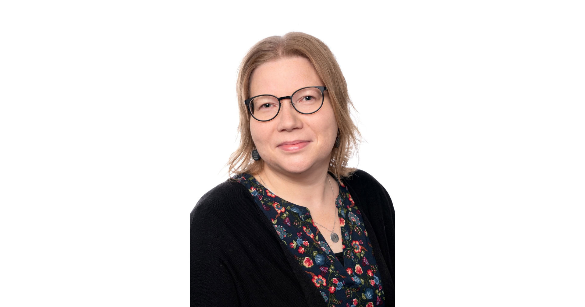 Kristiina Brisk‑Mosander katsoo kohti kameraa, päällään kuviollinen pusero, musta neuletakki ja silmälasit.