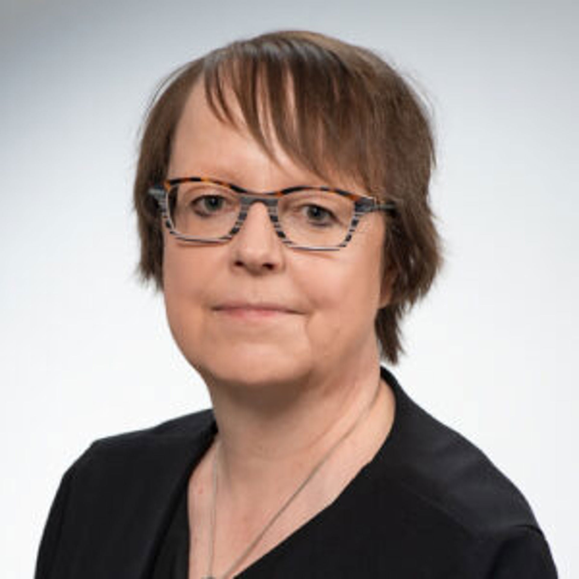 Tuula Oksanen katsoo kohti kameraa, päällään musta yläosa ja silmälasit.