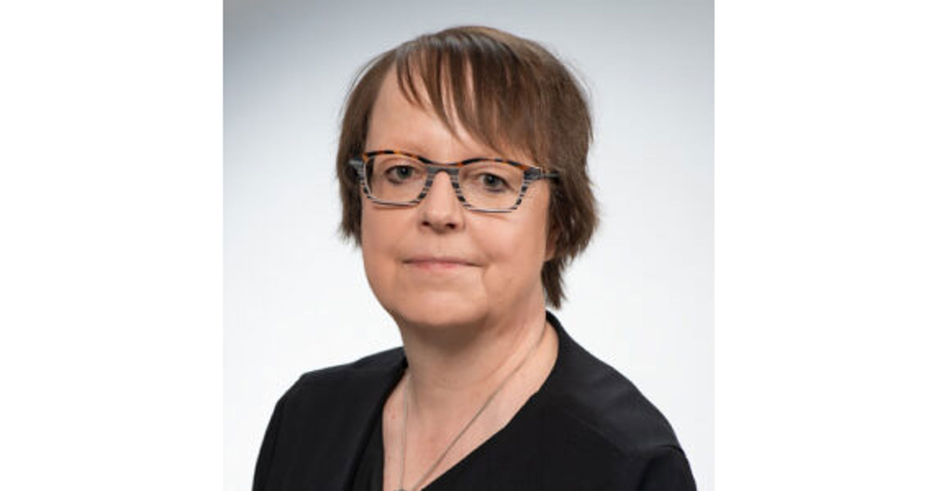 Tuula Oksanen katsoo kohti kameraa, päällään musta yläosa ja silmälasit.