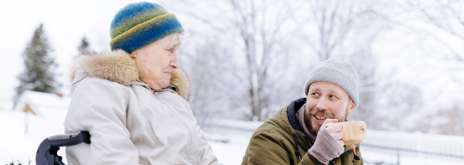 Kaksi henkilöä juttelevat ja juovat kupeista ulkona talvella.