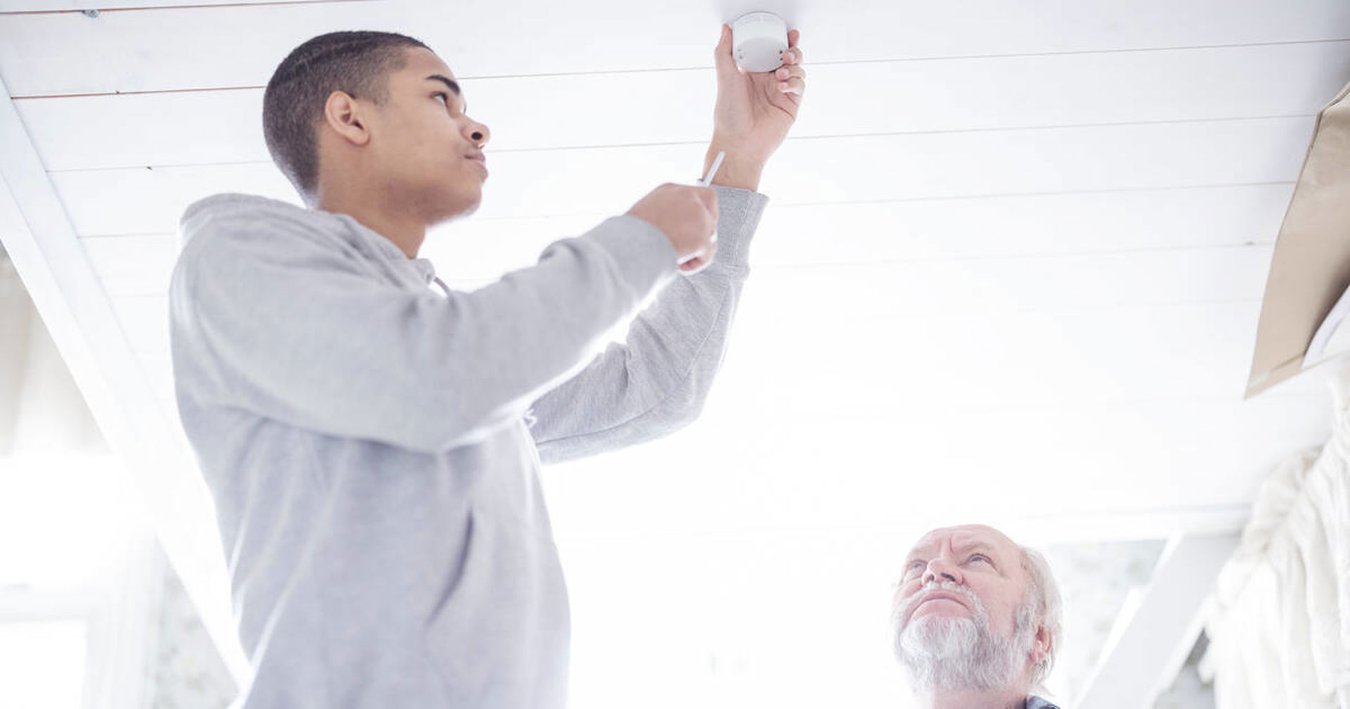 Nuori asentaa lamppua, kun vanhempi henkilö seuraa vierestä.