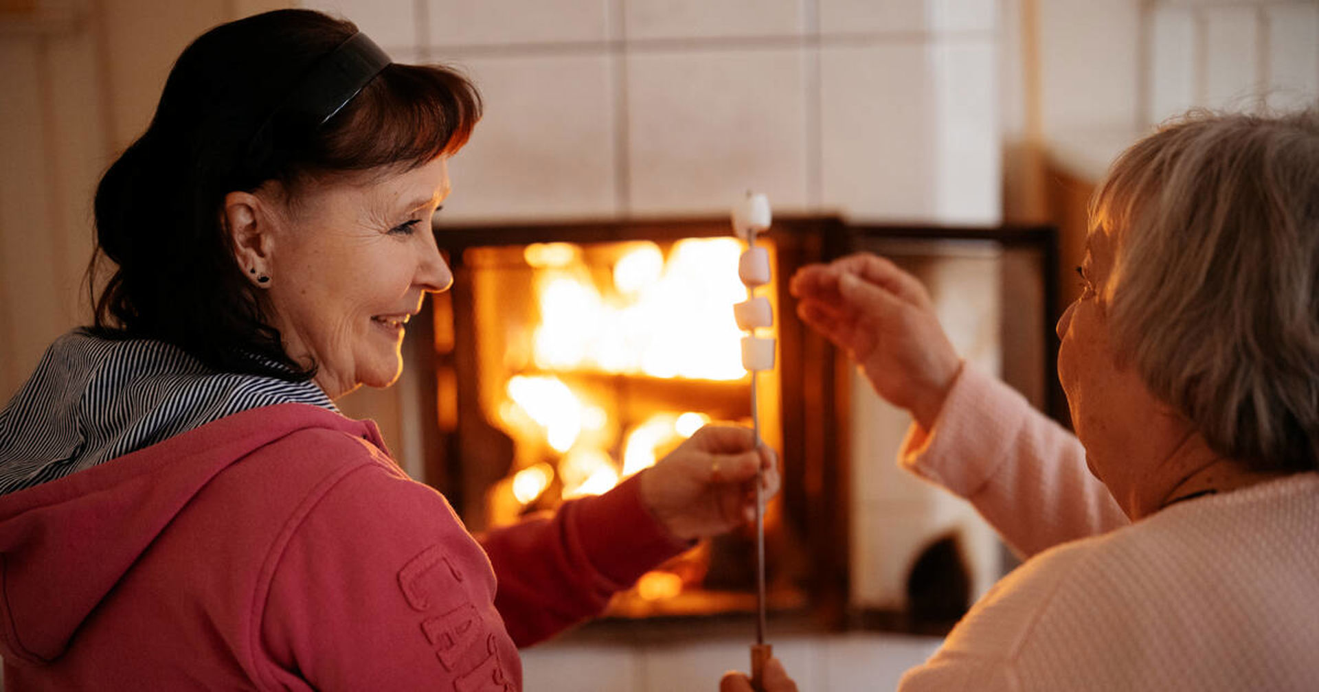 Kaksi henkilöä paahtaa vaahtokarkkeja takassa.