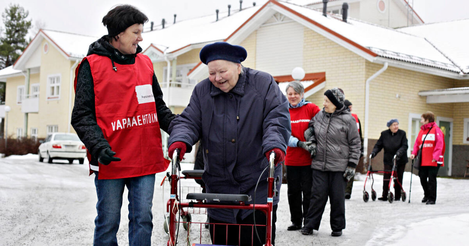Punaisen Ristin vapaaehtoisia vanhusten vierellä ulkona lähdössä jonossa palvelutalosta.